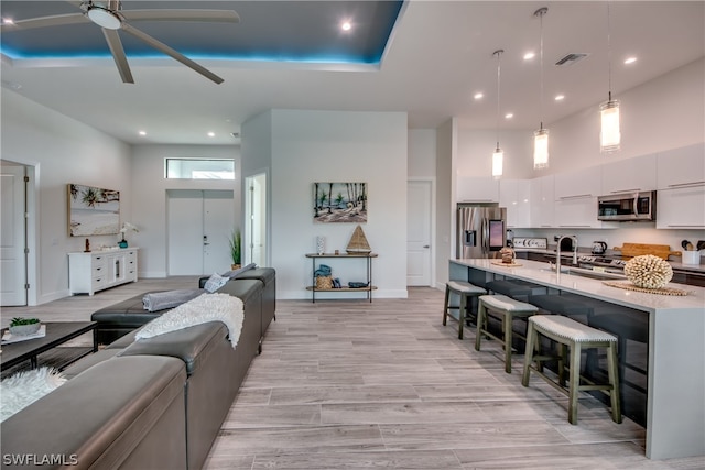 living room featuring sink, light hardwood / wood-style floors, ceiling fan, and a high ceiling