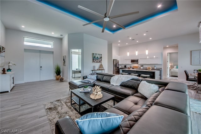 living room featuring light hardwood / wood-style flooring, ceiling fan, a tray ceiling, and a high ceiling