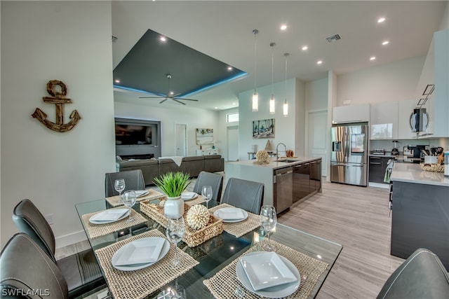 dining space featuring a raised ceiling, light hardwood / wood-style flooring, ceiling fan, and sink