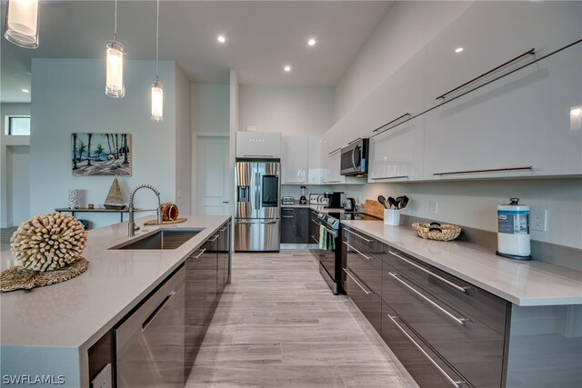 kitchen with decorative light fixtures, stainless steel appliances, light hardwood / wood-style floors, white cabinets, and sink