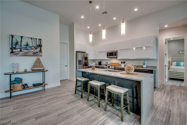 kitchen with appliances with stainless steel finishes, hanging light fixtures, light hardwood / wood-style floors, a kitchen island with sink, and sink