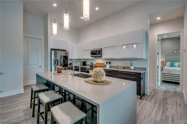 kitchen with a kitchen island with sink, a breakfast bar, hanging light fixtures, light wood-type flooring, and stainless steel appliances