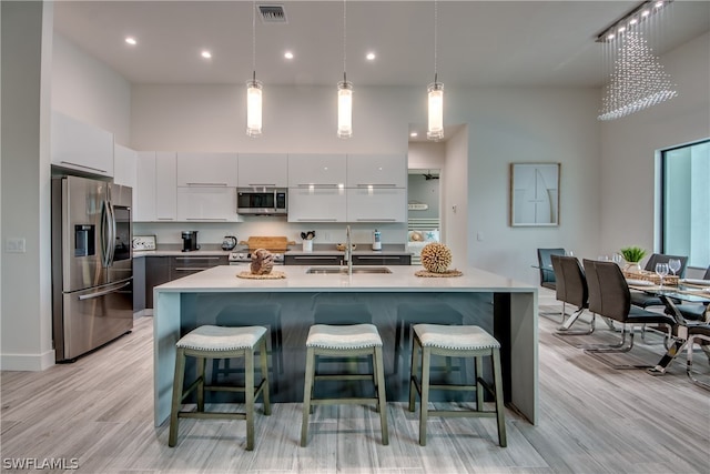 kitchen featuring a towering ceiling, sink, light hardwood / wood-style floors, hanging light fixtures, and stainless steel appliances