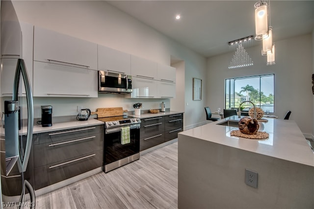 kitchen with appliances with stainless steel finishes, light hardwood / wood-style flooring, hanging light fixtures, white cabinets, and sink