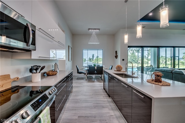 kitchen featuring decorative light fixtures, light hardwood / wood-style flooring, stainless steel appliances, sink, and an island with sink