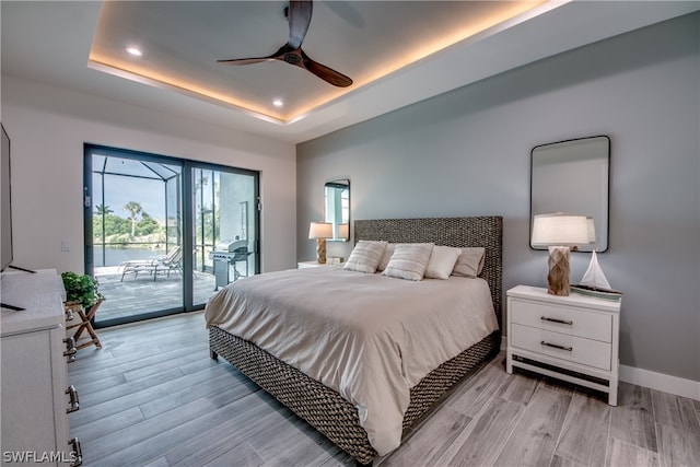 bedroom with access to outside, ceiling fan, light wood-type flooring, and a tray ceiling