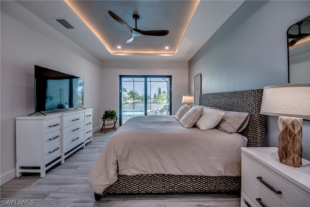 bedroom with light hardwood / wood-style flooring, ceiling fan, access to outside, and a raised ceiling