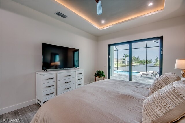 bedroom with access to exterior, wood-type flooring, ceiling fan, and a raised ceiling