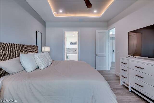 bedroom with wood-type flooring, ceiling fan, a raised ceiling, and ensuite bathroom