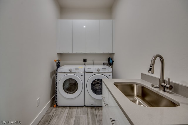 laundry area with sink, light hardwood / wood-style flooring, washer and dryer, and cabinets