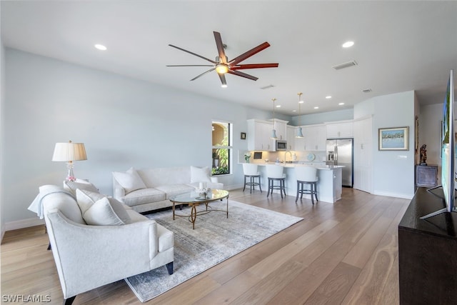 living room with ceiling fan, light hardwood / wood-style floors, and sink