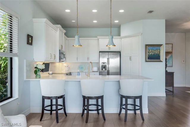 kitchen with stainless steel appliances, backsplash, hardwood / wood-style floors, white cabinetry, and pendant lighting