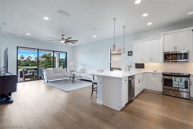 kitchen featuring light wood-type flooring, appliances with stainless steel finishes, kitchen peninsula, pendant lighting, and ceiling fan