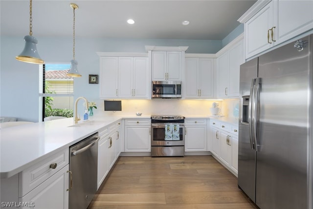 kitchen with light hardwood / wood-style flooring, kitchen peninsula, stainless steel appliances, sink, and white cabinetry