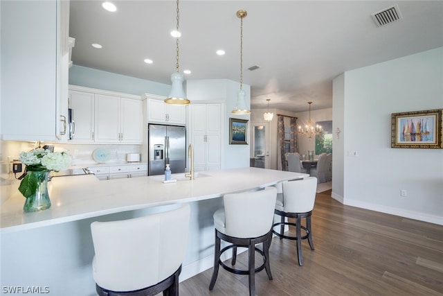 kitchen with stainless steel fridge, dark hardwood / wood-style flooring, white cabinets, a breakfast bar area, and pendant lighting