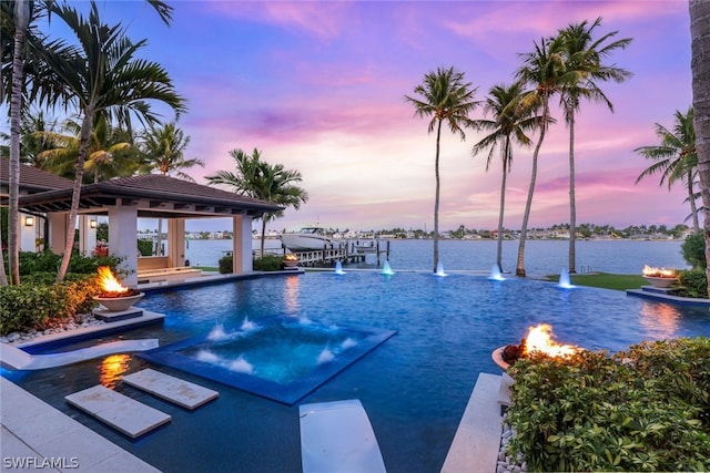 pool at dusk with pool water feature, a water view, and a dock