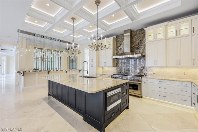 kitchen with a center island with sink, stainless steel appliances, white cabinets, wall chimney exhaust hood, and coffered ceiling