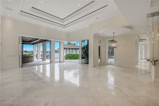 tiled spare room with a towering ceiling, a tray ceiling, crown molding, and a chandelier