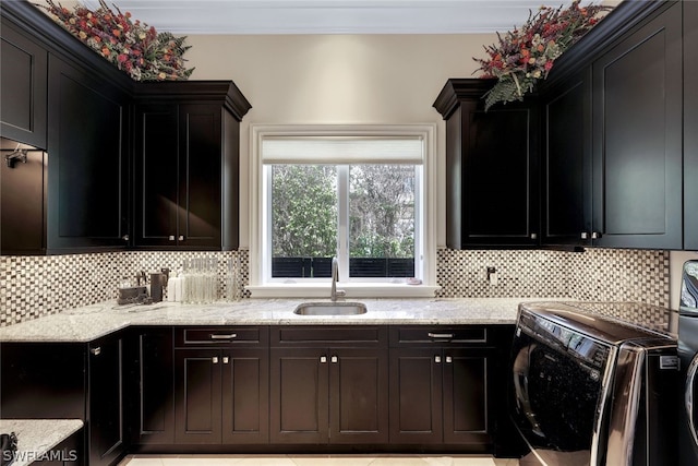 kitchen featuring light stone countertops, washing machine and dryer, sink, tasteful backsplash, and light tile floors