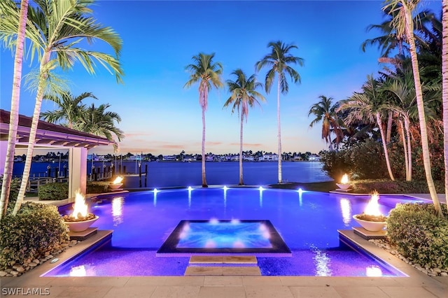 pool at dusk featuring a water view and an in ground hot tub