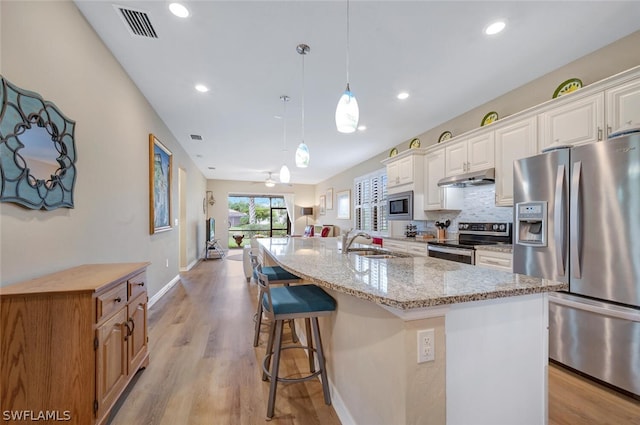 kitchen with light stone countertops, a center island with sink, light hardwood / wood-style flooring, and appliances with stainless steel finishes