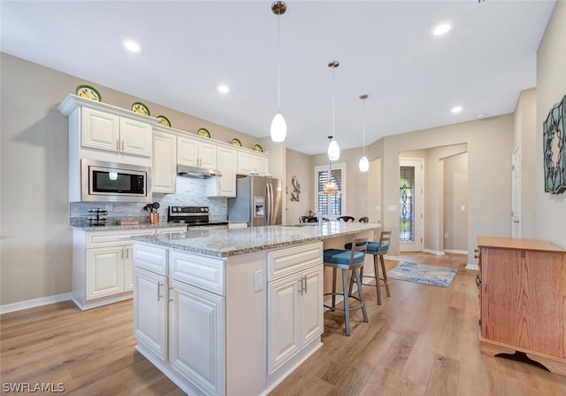 kitchen with light hardwood / wood-style floors, a kitchen island, hanging light fixtures, white cabinets, and appliances with stainless steel finishes