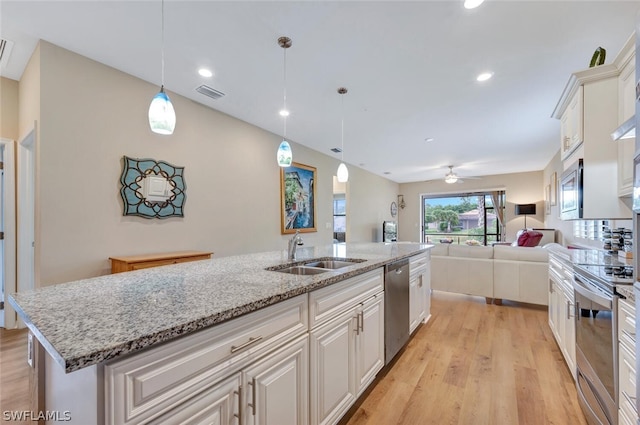 kitchen featuring light wood-type flooring, a center island with sink, stainless steel appliances, decorative light fixtures, and sink