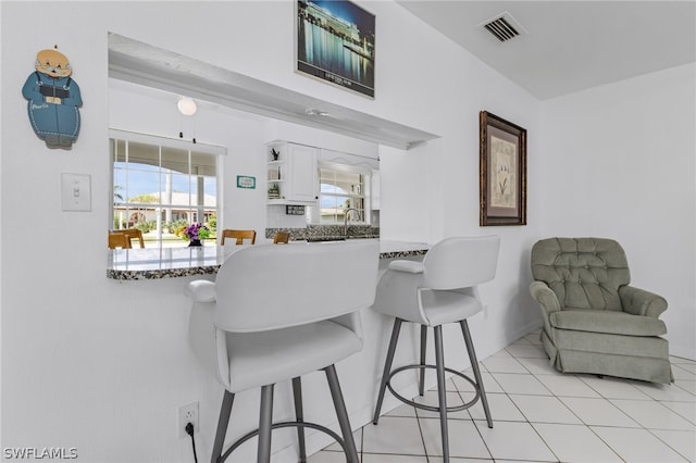 kitchen with white cabinets, light tile patterned flooring, a kitchen breakfast bar, and kitchen peninsula