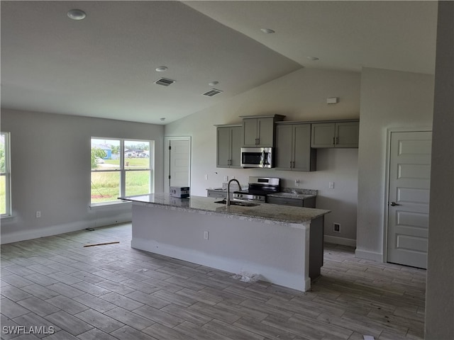 kitchen with appliances with stainless steel finishes, lofted ceiling, light wood-type flooring, and an island with sink