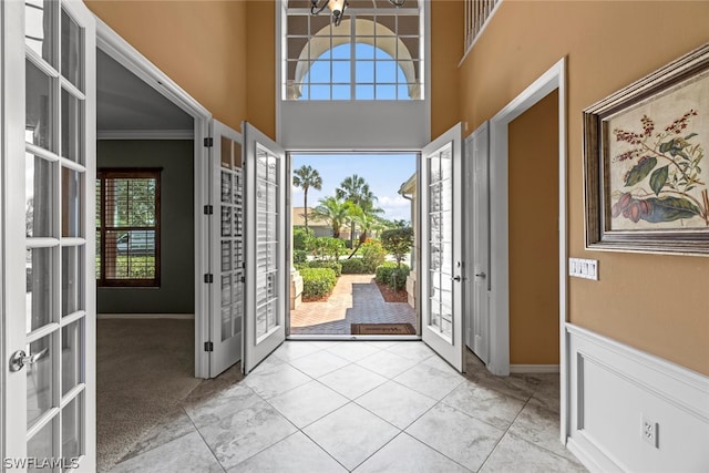 carpeted foyer entrance with french doors, a towering ceiling, and ornamental molding