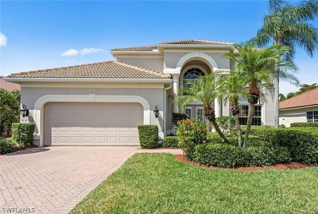 mediterranean / spanish house featuring a tiled roof, decorative driveway, an attached garage, and stucco siding