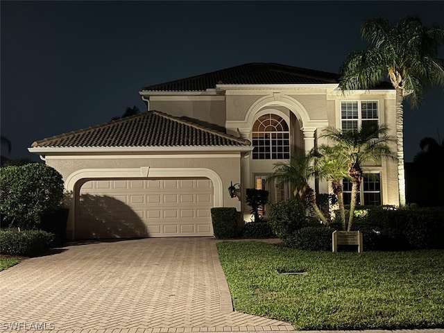 mediterranean / spanish house featuring a garage, a tile roof, decorative driveway, a yard, and stucco siding