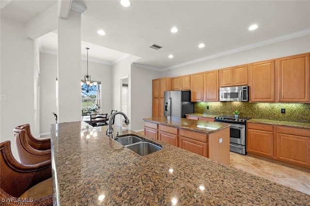 kitchen featuring pendant lighting, sink, a kitchen island with sink, stainless steel appliances, and dark stone counters