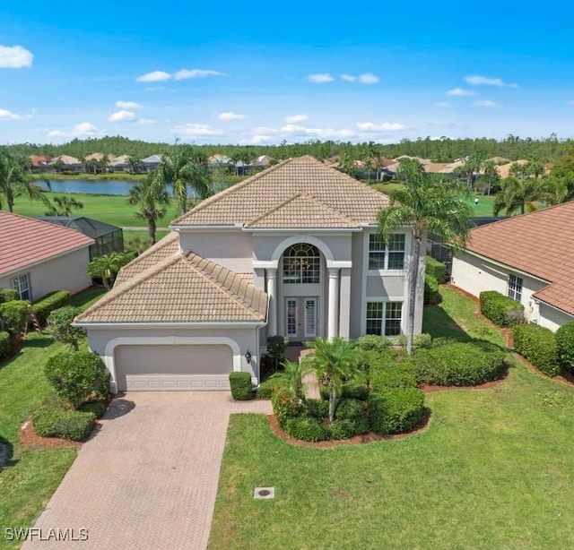 mediterranean / spanish home featuring decorative driveway, a tile roof, stucco siding, a water view, and a garage