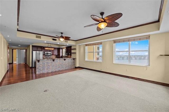 unfurnished living room with baseboards, a raised ceiling, crown molding, visible vents, and ceiling fan