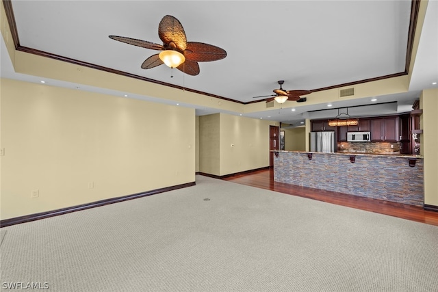 unfurnished living room with ceiling fan, ornamental molding, dark hardwood / wood-style flooring, and a tray ceiling