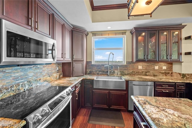 kitchen with dark wood-style flooring, ornamental molding, light stone counters, stainless steel appliances, and a sink