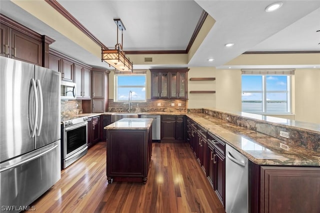 kitchen with ornamental molding, appliances with stainless steel finishes, a peninsula, and light stone countertops