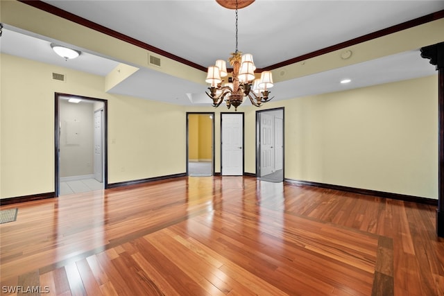 empty room with crown molding, a chandelier, and hardwood / wood-style flooring