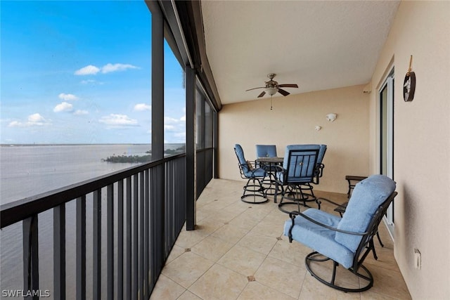 sunroom / solarium featuring tile patterned floors, ceiling fan, and a water view
