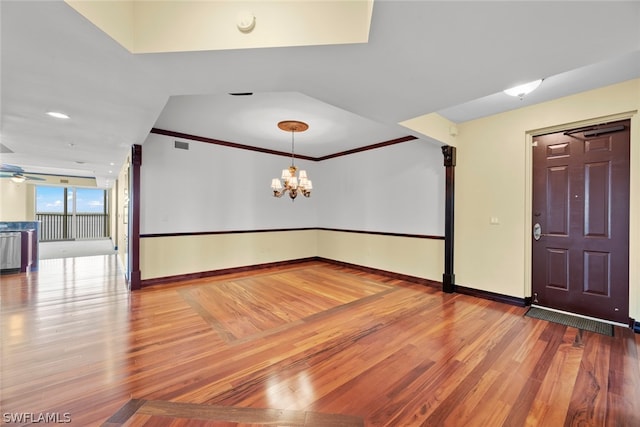 spare room with hardwood / wood-style floors, ceiling fan with notable chandelier, and ornamental molding