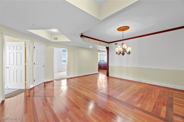 empty room featuring light wood-style floors, an inviting chandelier, baseboards, and ornamental molding
