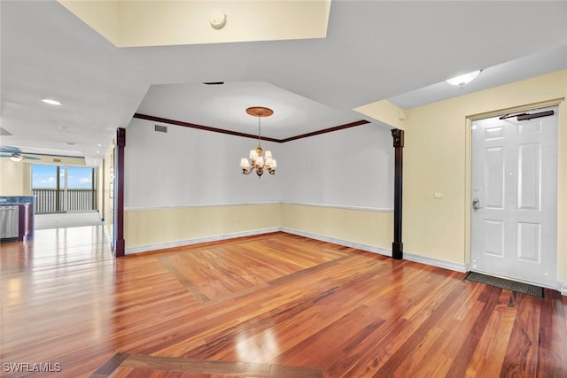 unfurnished room with crown molding, ceiling fan with notable chandelier, visible vents, wood finished floors, and baseboards