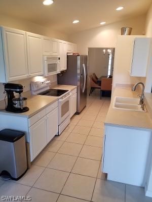 kitchen featuring light tile floors, white cabinetry, white appliances, and sink