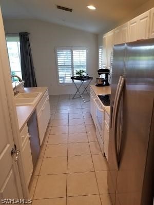 kitchen with a healthy amount of sunlight, stainless steel refrigerator, vaulted ceiling, sink, and light tile floors