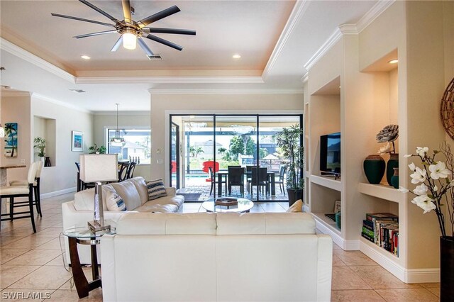 tiled living room with ceiling fan, built in features, crown molding, and a tray ceiling