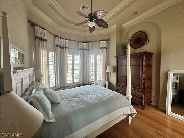 bedroom with wood-type flooring, a raised ceiling, ceiling fan, and ornamental molding