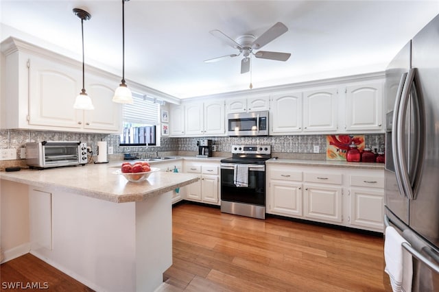 kitchen featuring white cabinets, decorative light fixtures, stainless steel appliances, light hardwood / wood-style flooring, and kitchen peninsula