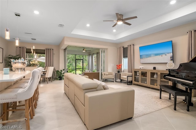 living room with light tile floors, ceiling fan, and a raised ceiling