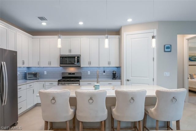 kitchen with appliances with stainless steel finishes, a center island with sink, white cabinets, and hanging light fixtures